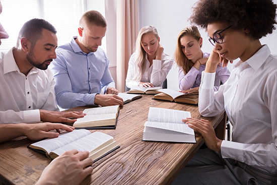 Cinco estudiantes multiraciales estudian la Biblia, cada uno con su Biblia abierta encima de una mesa, ilustración para Clases biblicas de textos sin ilustraciones.