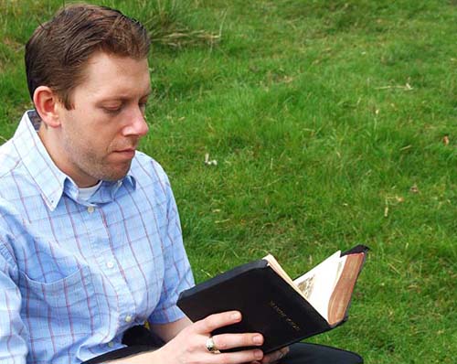 EThis photograph of a man reading the Bible in a rural setting of a green field illustrates the subject The Ideal Church, According to God, in editoriallapaz.org.