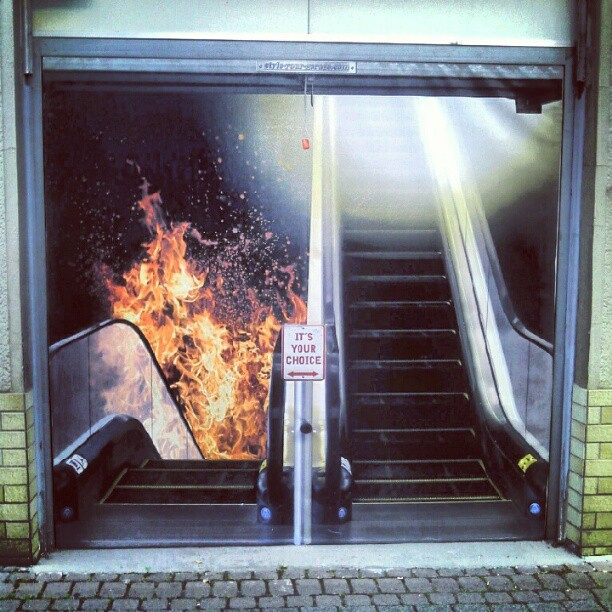 In this image, the escalator on the right leads up to a graphic symbolizing God’s Heaven, while the one on the left leads down toward bright flames representing Hell, and a sign in front of both says, with arrows: The decision is yours, an illustration for the subject: Alarming, Vivid and Unforgettable Impressions Registered by the Mind, a concise message for spiritual orientation.