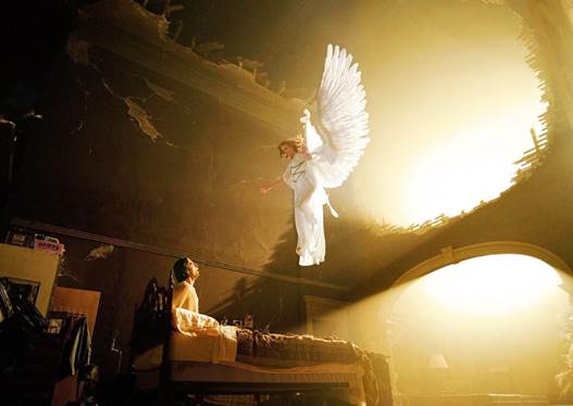 Una representación artística en colores de oro y marón de un ángel en blanco con alas blancas extendidas aparece en el espacio abstracto encima de una cama donde un enfermo lo mira intensamente.