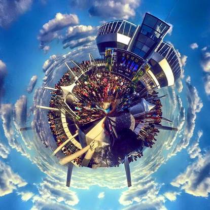 Una creación artística del globo terráqueo llena de seres humanos con ciudades y estructuras en la periferia del globo, rodeado el globo con nubecillas blancas contra el espacio azul.