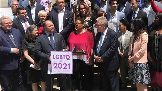 Una fotografía de un grupo de dignatarios políticos uno de los cuales sostiene delante de él una cartulina en apoyo de las coaliciones de arco iris.