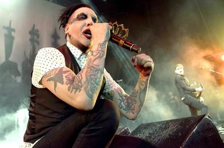 Una fotografía de cantante Marilyn Manson en el acto de cantar, muchos tatuajes visibles en sus brazos.