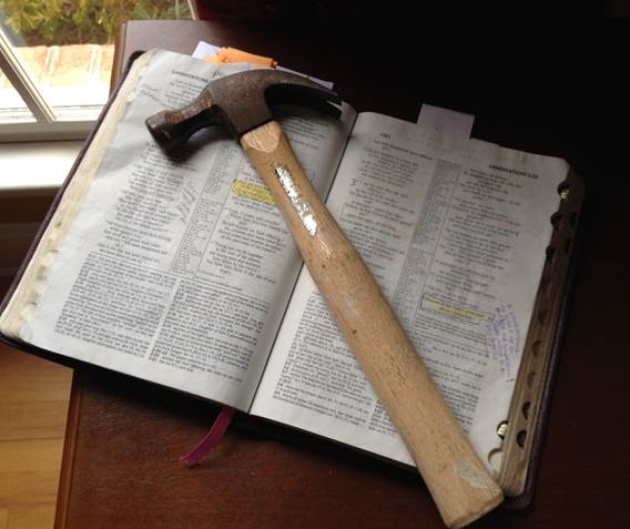 Imagen de un martillo colocado sobre una Biblia abierta, proyectándose el concepto de la Palabra de Dios en su función de martillo que hace añicos de supersticiones, vanas tradiciones, filosofías huecas y errores de toda categoría.