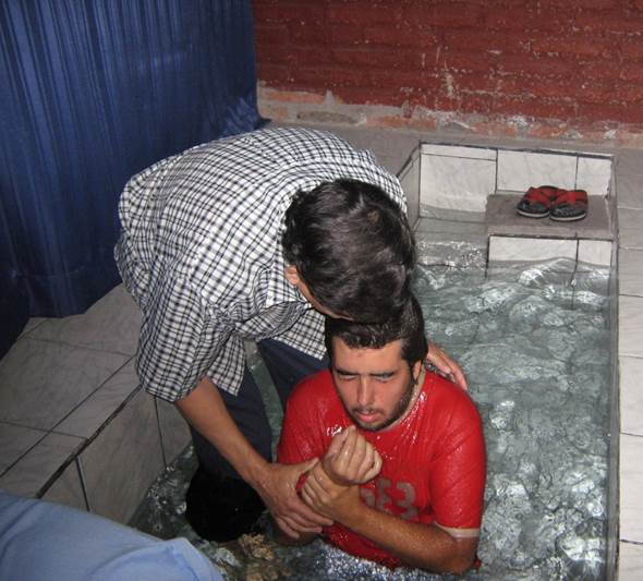 Fotografía del bautismo por inmersión de un varón en un bautisterio lleno de agua.