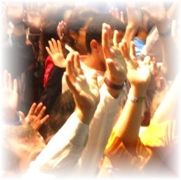 Una fotografia bien de cerca de los brazos y las manos de varios adoradores carismáticos levantados hacia arriba, manos que aportan diezmos.