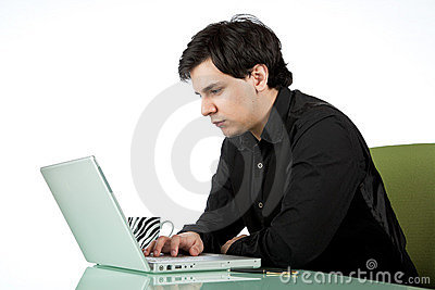Fotografía de un varón jóven sentado frente a una mesita con una laptop frente a él y una taza de café al lado.
