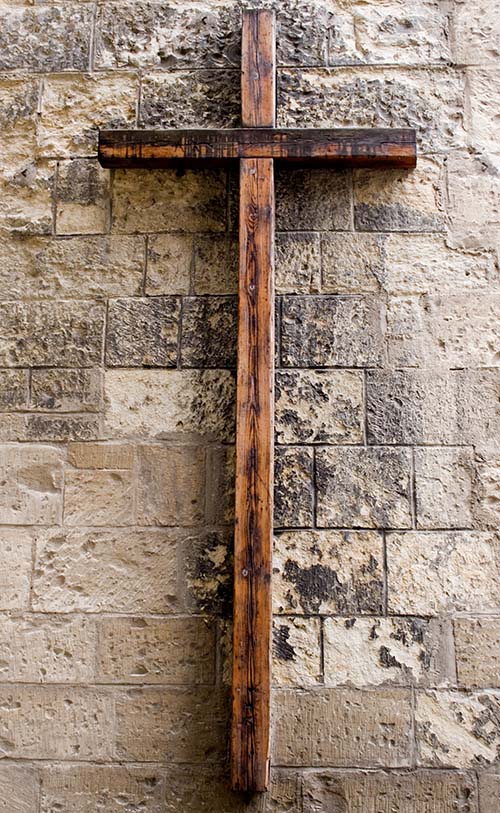 Esta fotografía de una cruz de madera sobre una pared de bloques ilustra el subtítulo La cruz como signo de superstición o símbolo de reconciliación, del mensaje La cruz no será más pesada que la gracia que él os da, en editoriallapaz.org.