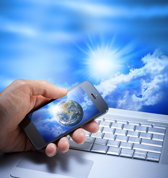 A hand holding a cellular phone with a globe of Earth on the screen, over a computer keyboard, against a background of sky, clouds and sun, illustrates the Report by Dewayne and Rita Shappley, for April, 2013, on their evangelistic work for the Lord and His church.
