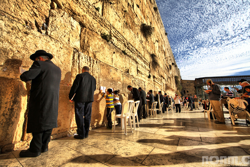 The late evening sun illuminates the Western Wall, or Wailing Wall, as some Jews stand close to it, a photograph illustrating the subject Jews Today: Missing Out?