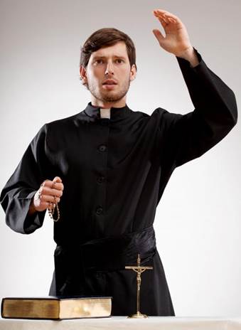 Fotografía de un sacerdote católico romano con el brazo izquierdo levantado, un rosario en la mana derecha, una Biblia cerrada y un crucifijo en una mesa delante de él, contra un trasfondo de púrpura claro.