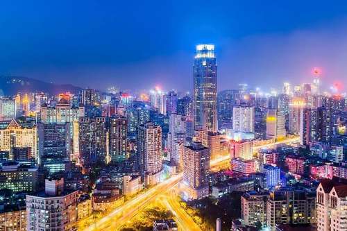 Una fotografía de una enorme ciudad del siglo XXI con rascacielos, otros edificios y calles alumbradas.