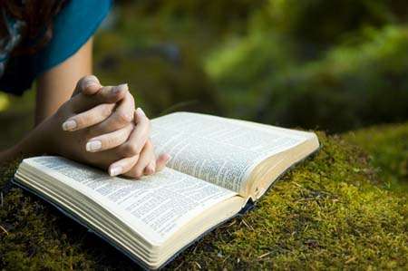 Esta fotografía de la Biblia abierta sobre grama verde, con manos femeninas encima, ilustra el Intercambio sobre el don del Espíritu Santo, fe, bautismo y nacer de nuevo, en editoriallapaz.